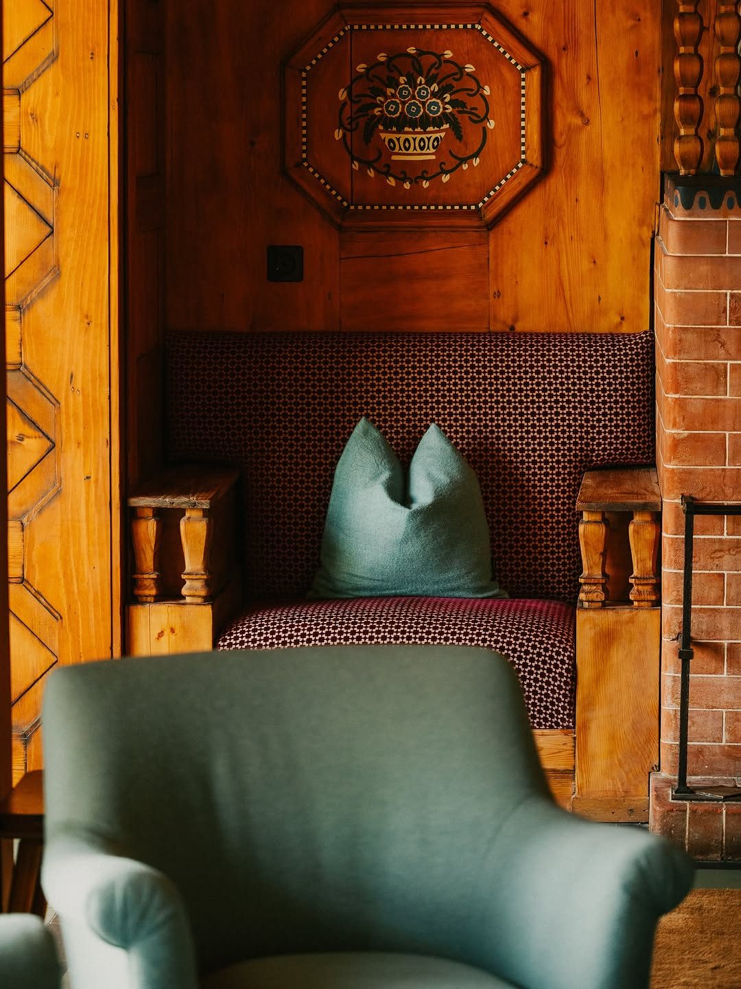 A carved wooden bench with patterned red upholstery and a mint wool cushion